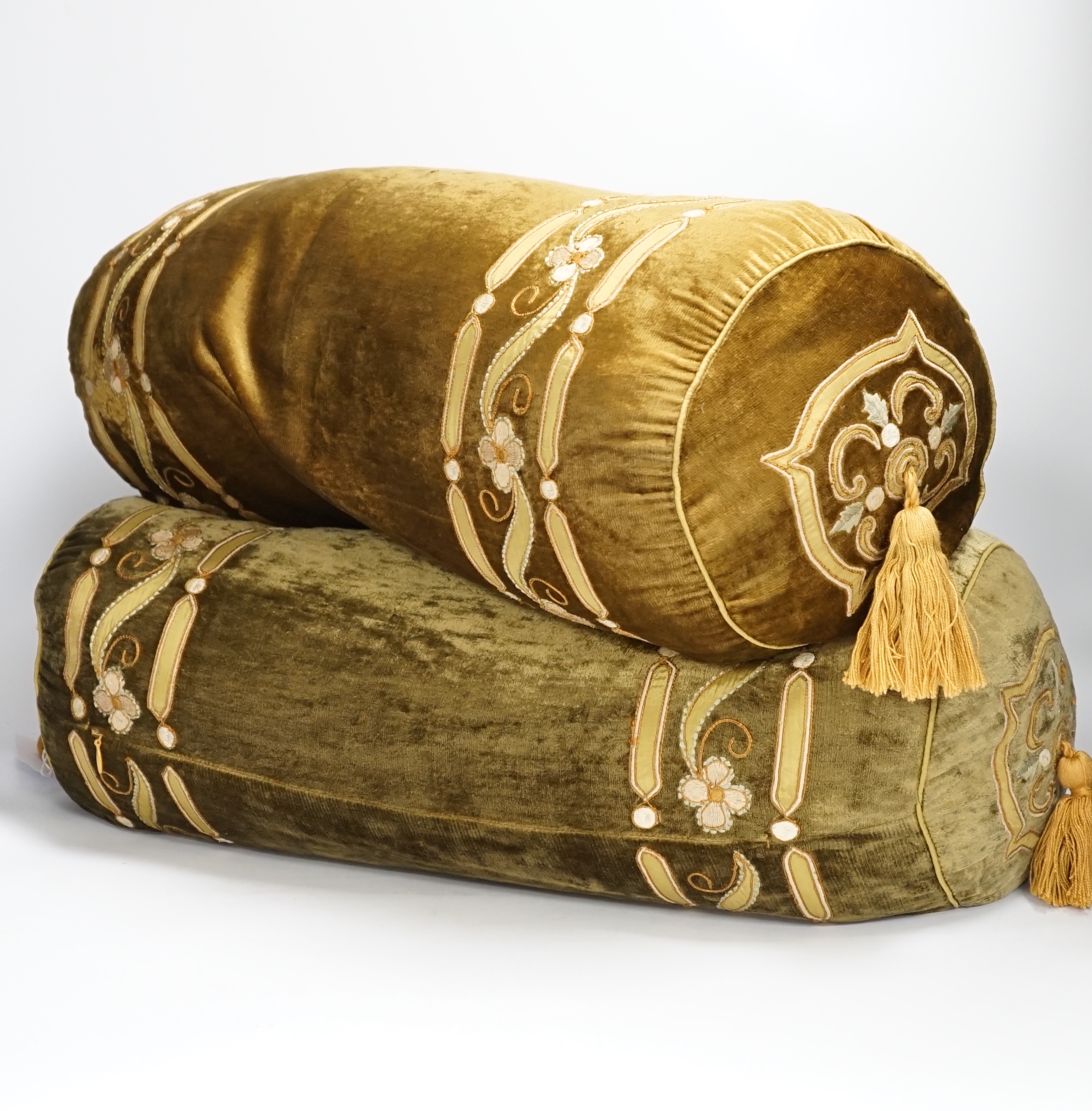 A pair of 20th century olive green silk velvet bolster cushions designed with appliqué, embroidered decoration and cording, finished with gold tassels to each end, 52cms long